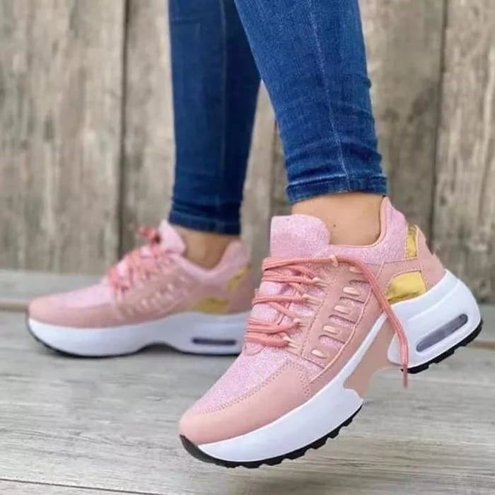 Women's sneakers in pink with gold accents, worn by a person in blue jeans. Fashionable sneakers, ideal for leisure and sport.