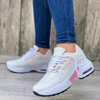 White women's sneakers with pink accents, worn by a person in blue jeans. Fashionable sneakers, ideal for leisure and sport.