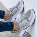 Gray women's sneakers with white sole, mesh upper and laces, worn with blue jeans and a gold anklet.